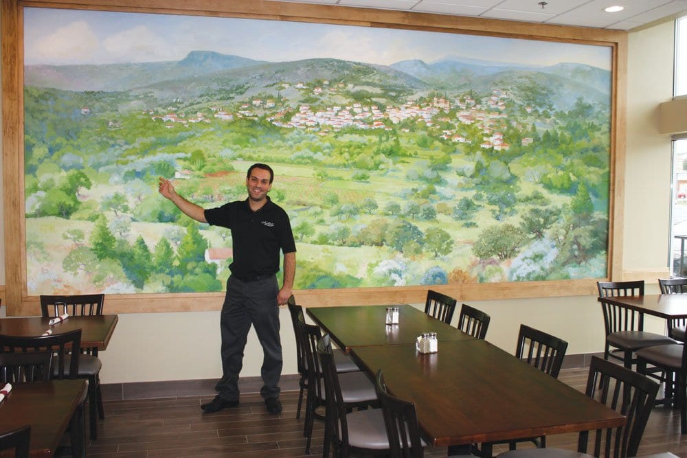 peter zoutis, GENERAL MANAGER of ANTHONY’S and son-in-law of owners Tony and Faye Yianiarrakis points to the home he grew up in, visible in a mural at the restaurant painted by Alexia Scott depicting the village of Niata in southern Greece, where both Faye and Peter are from. (Photo: News-Press)