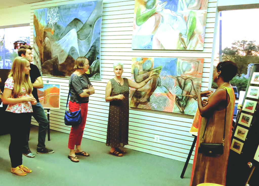 Painter Susan Grace (center) talks about one of her new works of art during the First Friday festivities last week. Grace’s work, the latest of which was inspired by the mountains of West Virginia, is currently on display at Art and Frame of Falls Church. The exhibit will be on display through the end of September. (Photo: Courtesy of Shaun Van Steyn)